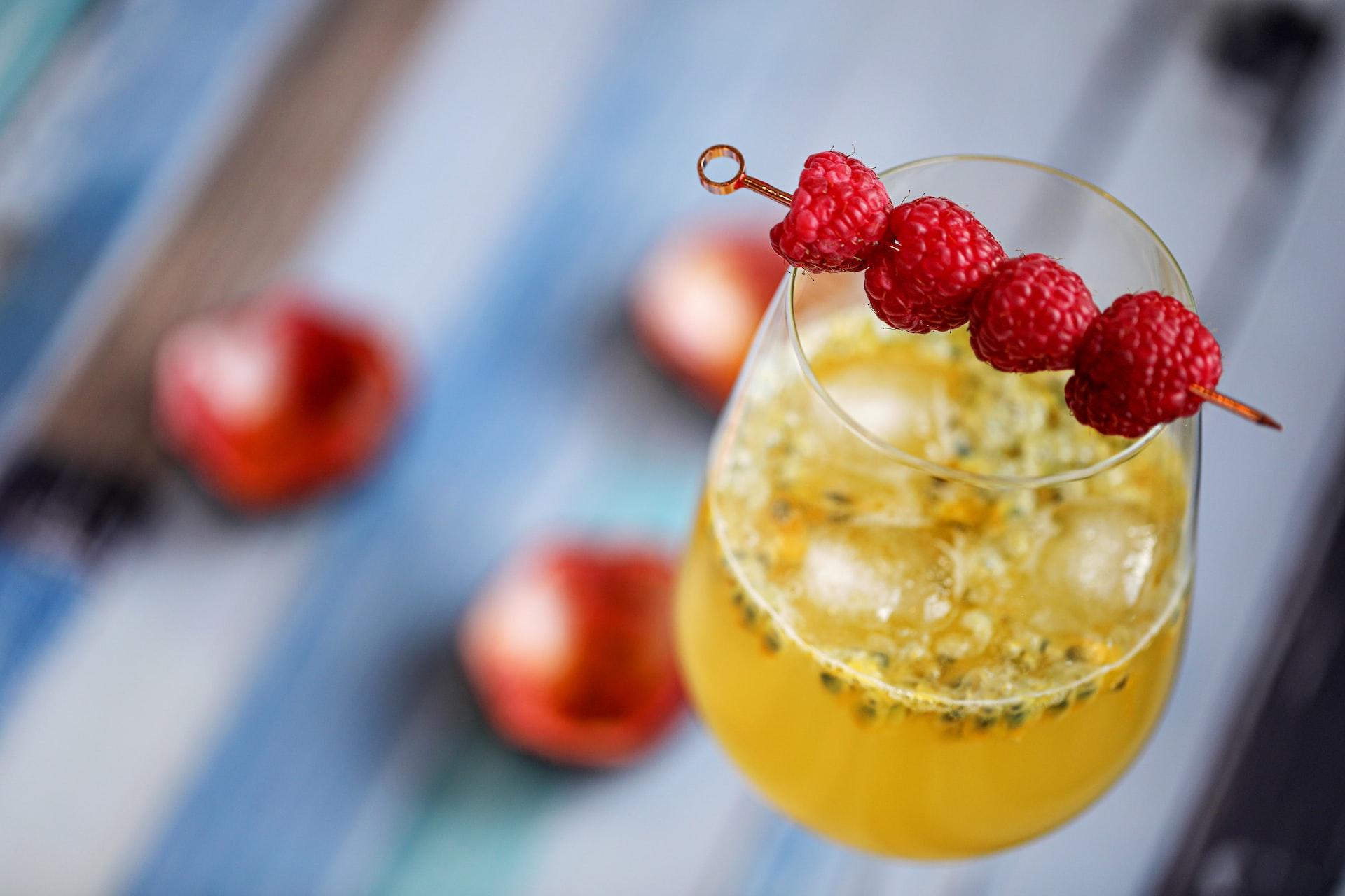 a glass of yellow liquid with red berries on top
