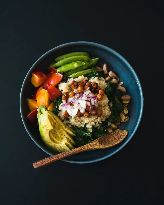 a blue bowl filled with vegetables and a wooden spoon